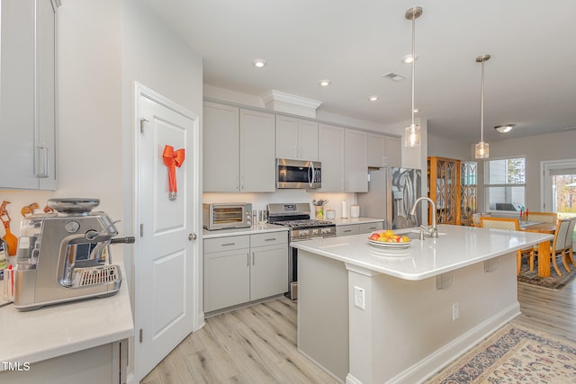 kitchen with appliances with stainless steel finishes, gray cabinetry, a center island with sink, light hardwood / wood-style flooring, and hanging light fixtures