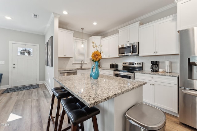 kitchen featuring stainless steel appliances, white cabinetry, light wood-type flooring, backsplash, and hanging light fixtures