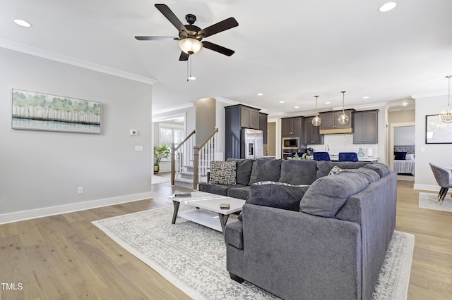 living room with light wood-type flooring, ceiling fan with notable chandelier, and ornamental molding