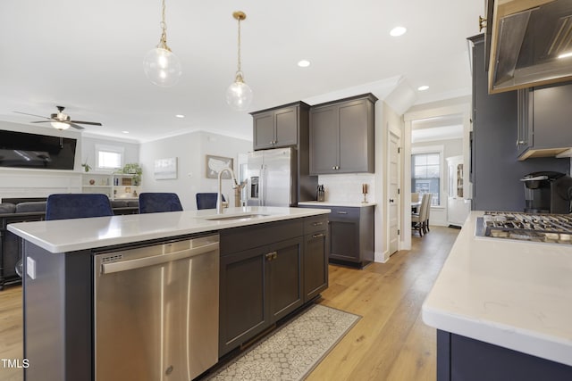 kitchen with appliances with stainless steel finishes, ceiling fan, a kitchen island with sink, sink, and pendant lighting