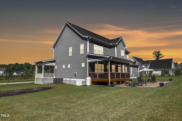 back house at dusk with a patio area, a yard, and central AC unit