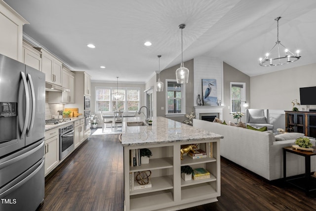 kitchen featuring light stone counters, hanging light fixtures, an island with sink, and stainless steel appliances