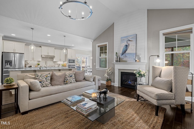 living room featuring high vaulted ceiling, sink, dark hardwood / wood-style floors, a fireplace, and a chandelier