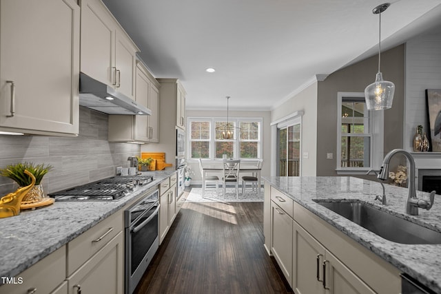 kitchen with light stone counters, stainless steel appliances, dark wood-type flooring, sink, and pendant lighting