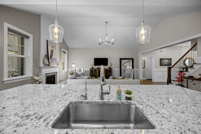 kitchen with light stone counters, lofted ceiling, sink, and hanging light fixtures