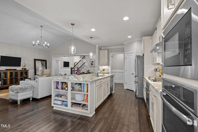 kitchen with light stone counters, a center island with sink, decorative light fixtures, and appliances with stainless steel finishes