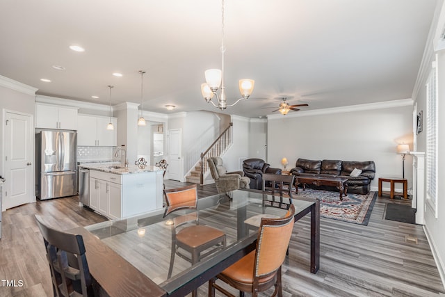 dining area with ornamental molding, light wood-type flooring, ceiling fan with notable chandelier, and sink