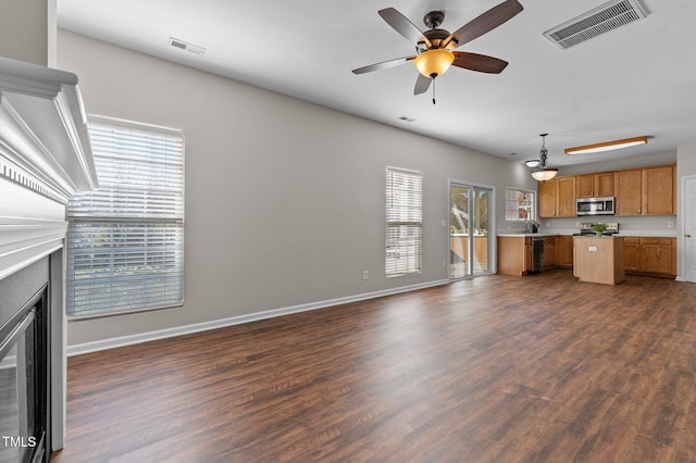 unfurnished living room featuring ceiling fan, a healthy amount of sunlight, and dark hardwood / wood-style floors