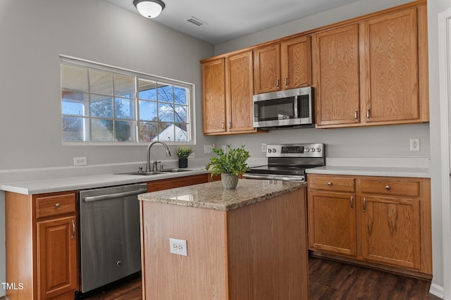 kitchen featuring sink, appliances with stainless steel finishes, dark hardwood / wood-style flooring, a kitchen island, and light stone counters