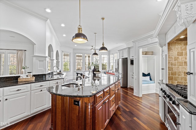 kitchen with a sink, appliances with stainless steel finishes, dark stone counters, dark wood finished floors, and a center island with sink