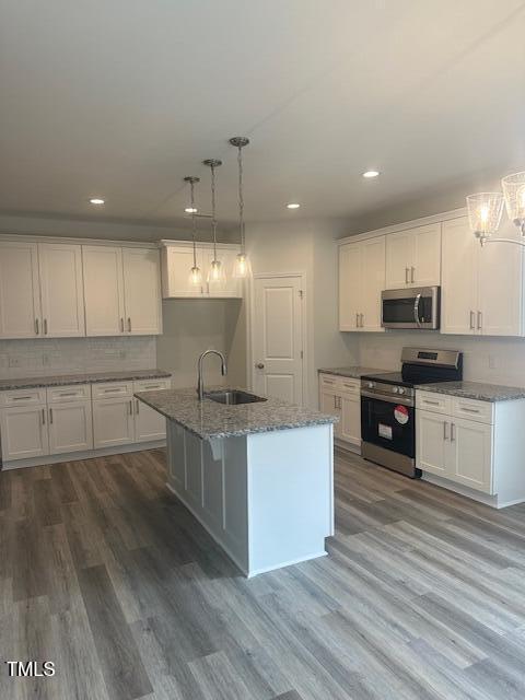 kitchen with white cabinetry, sink, hanging light fixtures, an island with sink, and appliances with stainless steel finishes