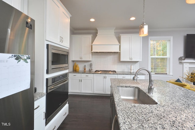 kitchen with white cabinetry, appliances with stainless steel finishes, sink, and premium range hood