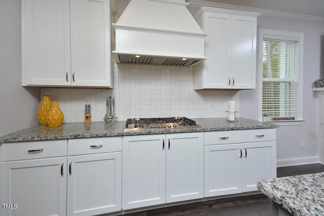 kitchen with custom range hood, white cabinetry, stainless steel gas stovetop, and decorative backsplash