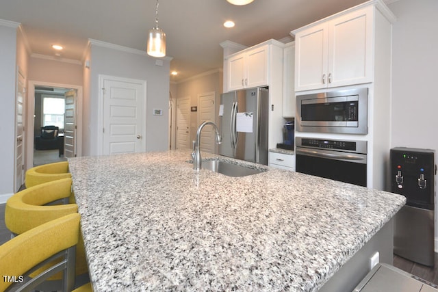 kitchen featuring a center island with sink, ornamental molding, stainless steel appliances, white cabinetry, and sink