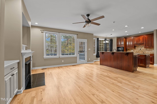 5600 Thornburg Dr, Wake Forest, NC 27587 - kitchen with ceiling fan, a kitchen breakfast bar, a fireplace with flush hearth, light wood-style flooring, and decorative backsplash