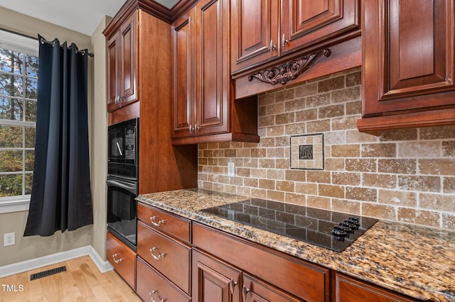 kitchen featuring decorative backsplash, light hardwood / wood-style floors, dark stone countertops, and black appliances