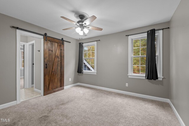 unfurnished bedroom featuring carpet, ceiling fan, a barn door, and multiple windows