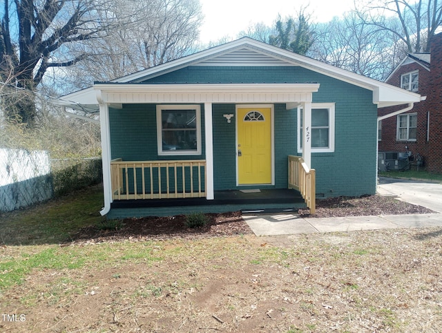 bungalow-style home featuring covered porch, brick siding, and fence