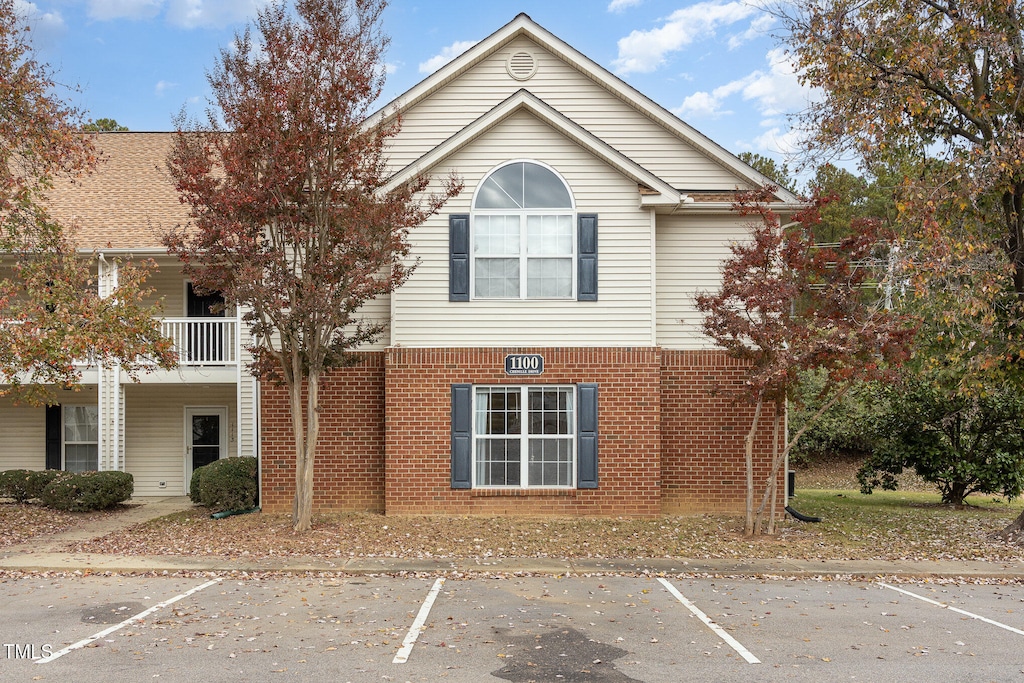 view of front of property with uncovered parking, brick siding, and a balcony