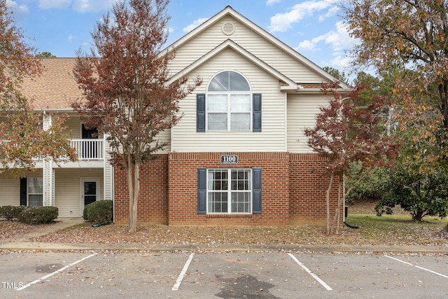 view of front of property with uncovered parking, brick siding, and a balcony