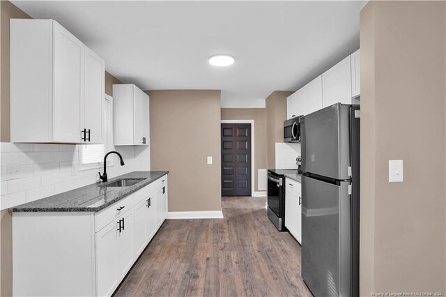 kitchen with stainless steel appliances, dark stone counters, white cabinetry, dark hardwood / wood-style floors, and sink