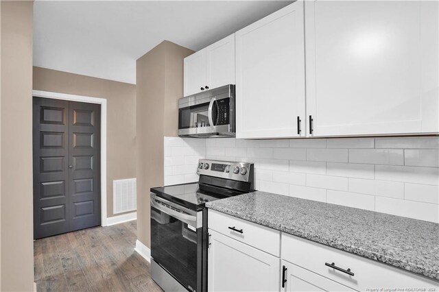 kitchen featuring wood-type flooring, light stone counters, backsplash, appliances with stainless steel finishes, and white cabinets