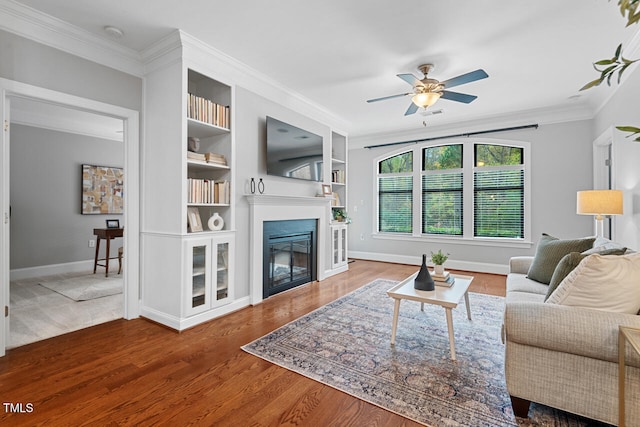 living room featuring ornamental molding, hardwood / wood-style floors, built in shelves, and ceiling fan