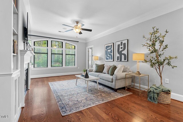 living area featuring ceiling fan, ornamental molding, baseboards, wood finished floors, and a fireplace
