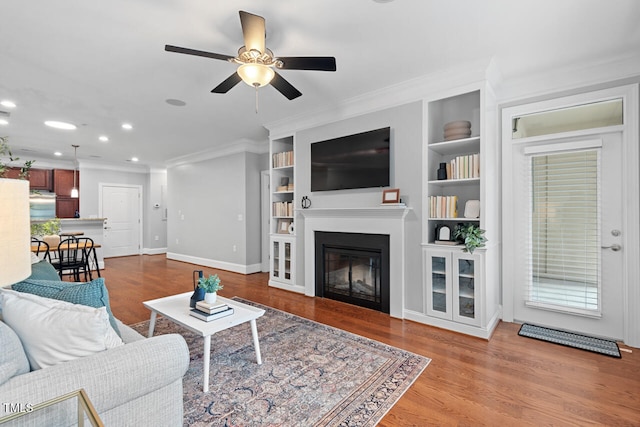 living room with built in shelves, light hardwood / wood-style flooring, ceiling fan, and crown molding