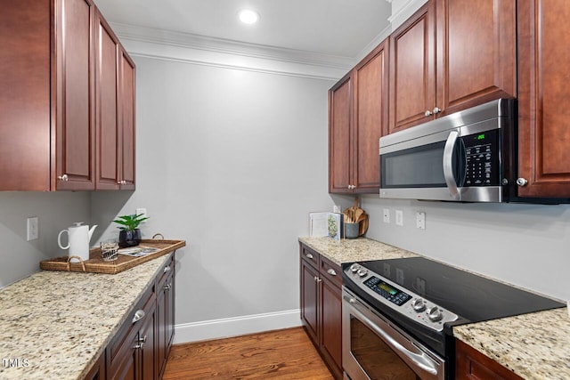 kitchen featuring appliances with stainless steel finishes, light wood-style flooring, ornamental molding, baseboards, and light stone countertops