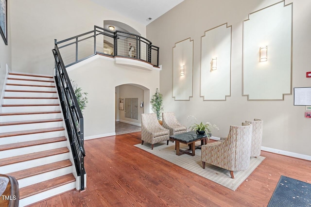 entryway featuring arched walkways, wood finished floors, baseboards, a high ceiling, and stairway