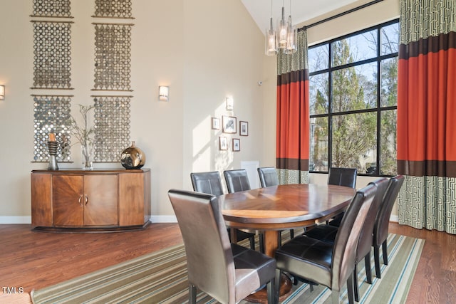 dining space with dark wood-type flooring, high vaulted ceiling, and a notable chandelier