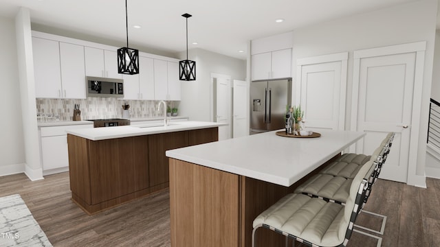 kitchen with a center island with sink, white cabinets, dark hardwood / wood-style floors, appliances with stainless steel finishes, and decorative light fixtures