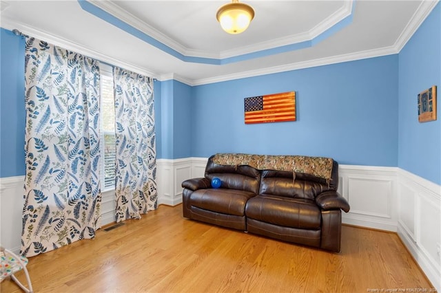 living room with a raised ceiling, ornamental molding, and light hardwood / wood-style flooring