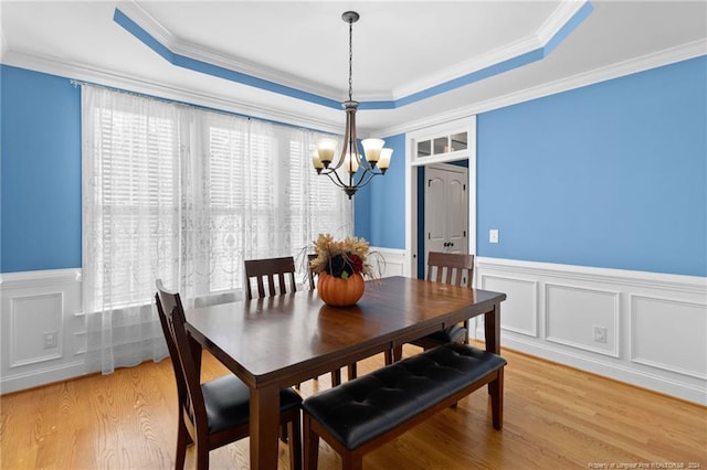 dining area with light hardwood / wood-style floors, an inviting chandelier, crown molding, and a tray ceiling