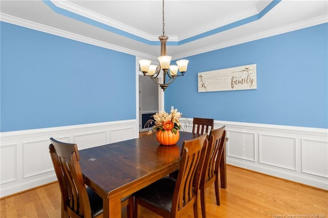 dining space with light hardwood / wood-style flooring, a chandelier, crown molding, and a raised ceiling