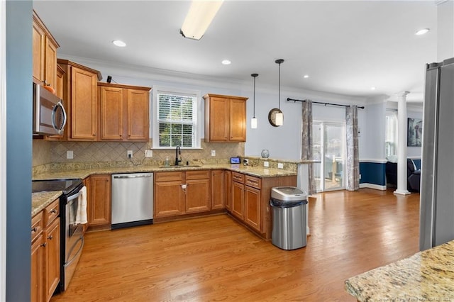 kitchen featuring appliances with stainless steel finishes, pendant lighting, decorative columns, kitchen peninsula, and light hardwood / wood-style flooring