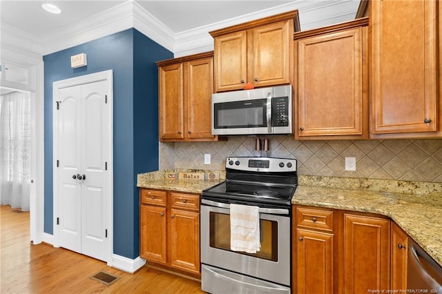 kitchen with light hardwood / wood-style floors, tasteful backsplash, crown molding, light stone countertops, and appliances with stainless steel finishes