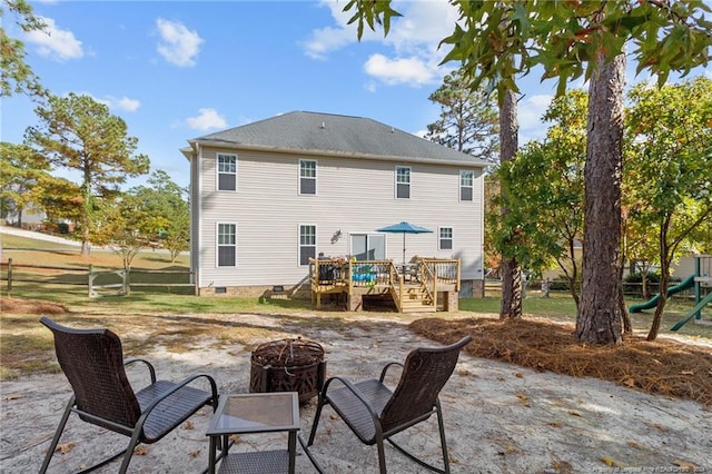 back of property with a deck, a patio, a playground, and an outdoor fire pit