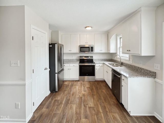 kitchen featuring light stone counters, white cabinetry, appliances with stainless steel finishes, dark hardwood / wood-style flooring, and sink