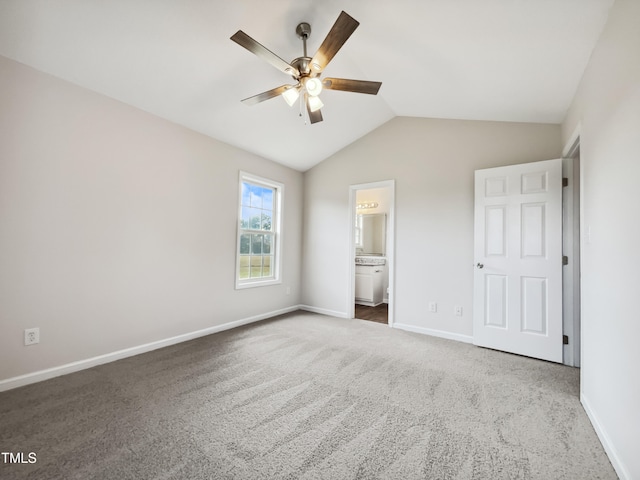 unfurnished bedroom with connected bathroom, lofted ceiling, dark carpet, and ceiling fan