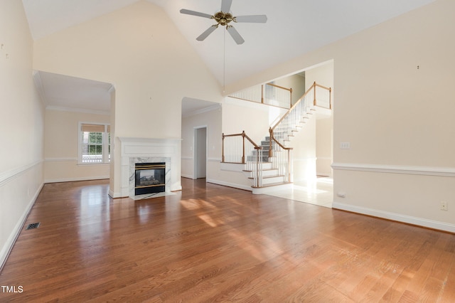 unfurnished living room featuring a high end fireplace, wood-type flooring, high vaulted ceiling, and ceiling fan