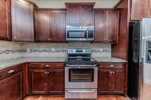 kitchen with backsplash, light stone counters, light hardwood / wood-style floors, and stainless steel appliances