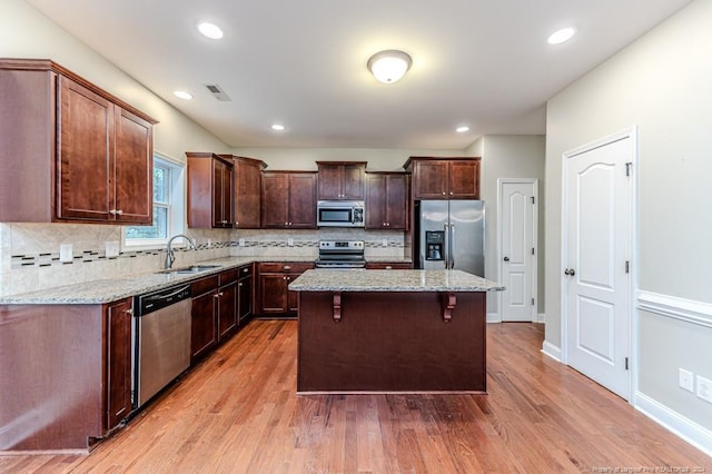 kitchen featuring light hardwood / wood-style floors, a center island, sink, light stone countertops, and appliances with stainless steel finishes