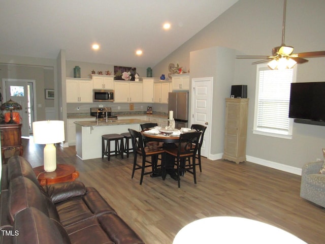 dining area with ceiling fan, wood-type flooring, sink, and high vaulted ceiling