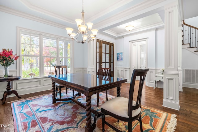 dining space with ornamental molding, a notable chandelier, dark hardwood / wood-style floors, a raised ceiling, and decorative columns