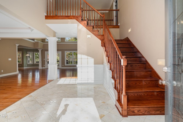 stairs featuring ornate columns, a towering ceiling, and wood-type flooring