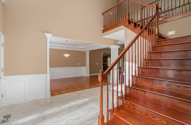 stairs with a towering ceiling, crown molding, a raised ceiling, hardwood / wood-style flooring, and decorative columns