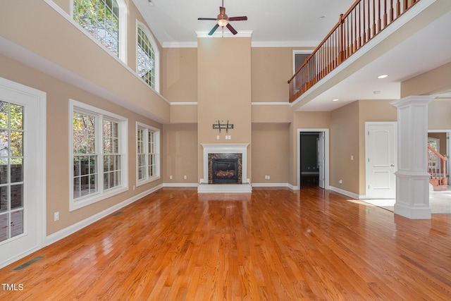 unfurnished living room featuring a towering ceiling, light wood-type flooring, and decorative columns