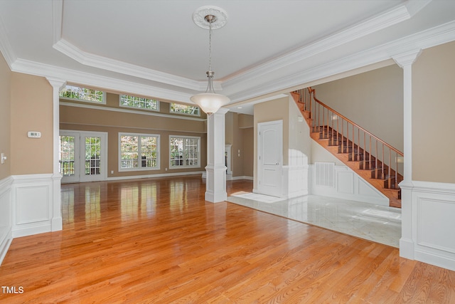 unfurnished living room featuring light hardwood / wood-style flooring, a tray ceiling, crown molding, and decorative columns